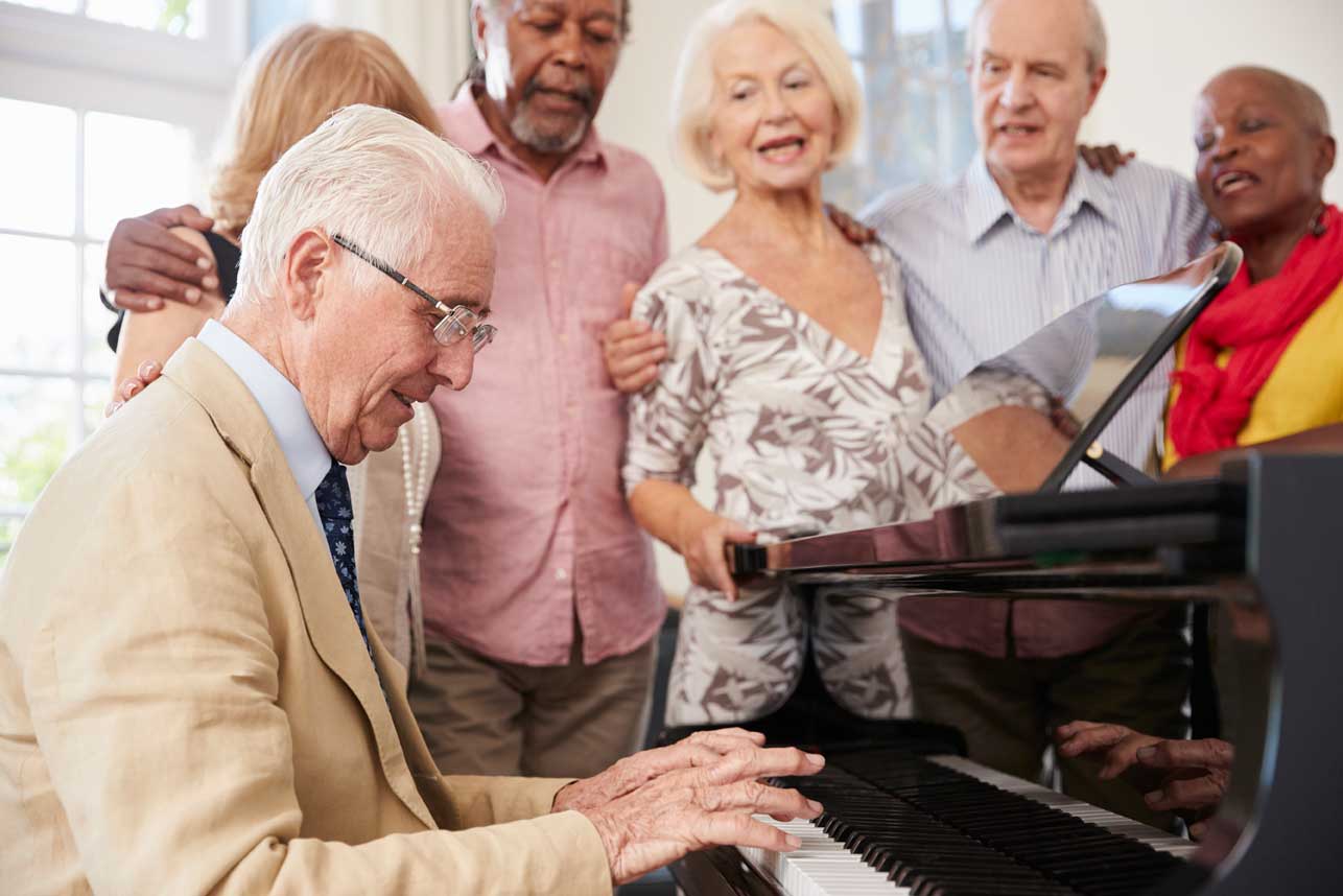 A group of older adults singing together around a piano